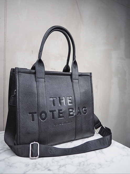 italienische mode kleiber werksverkauf Schwarze Einkaufstasche aus Leder mit der Prägung „The Tote Bag“ auf der Vorderseite.