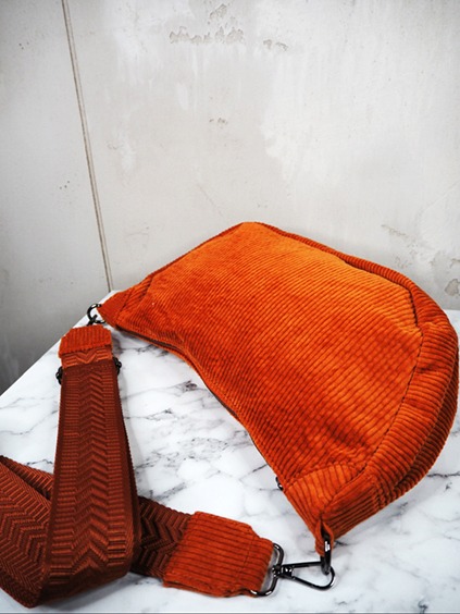 italienische mode kleiber werksverkauf Orangefarbene Cord-Umhängetasche mit gemustertem Riemen auf Marmoroberfläche.