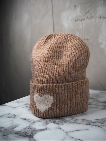 italienische mode kleiber werksverkauf Hellbraune gestrickte Wintermütze mit Herzdesign auf Marmoroberfläche.
