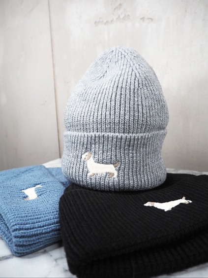italienische mode kleiber werksverkauf Graue Strickmütze mit aufgesticktem Dackel, blaue und schwarze Mützen im Hintergrund