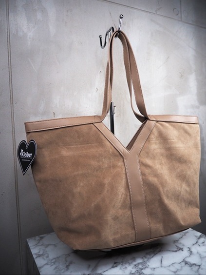 italienische mode kleiber werksverkauf Beige Kleiber-Einkaufstasche aus Wildleder mit Akzenten aus hellbraunem Leder, an einem Haken hängend.