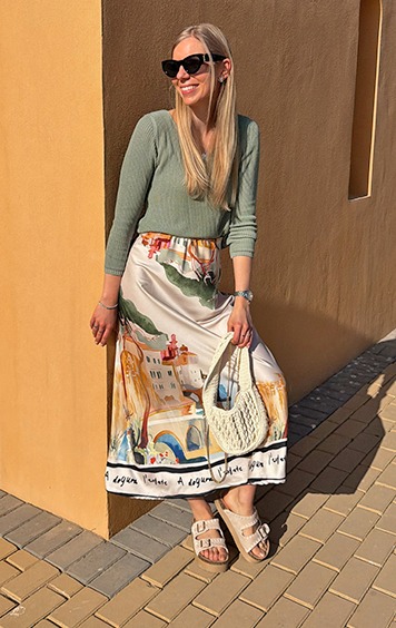 italienische mode kleiber werksverkauf Frau in grünem Oberteil und bedrucktem Rock mit Tasche und Sandalen