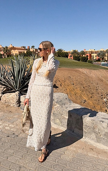 italienische mode kleiber werksverkauf Frau in einem weißen Kleid mit Sonnenbrille steht auf einem Weg mit Blick auf Gebäude