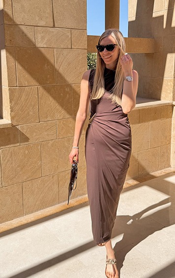 italienische mode kleiber werksverkauf Frau in braunem Kleid mit Sonnenbrille und Tasche vor Steingebäude