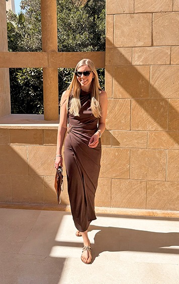 italienische mode kleiber werksverkauf Frau in braunem Wickelkleid mit Sonnenbrille und Tasche im Freien