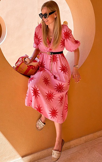 italienische mode kleiber werksverkauf Frau in rosa Kleid mit Sonnendruck sitzt auf orangefarbener Wand