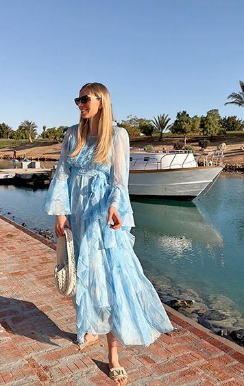 italienische mode kleiber werksverkauf Frau in blauem Rüschenkleid am Wasser mit Boot