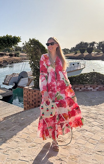 italienische mode kleiber werksverkauf Frau in einem blumigen Maxikleid mit Stroh-Handtasche am Wasser