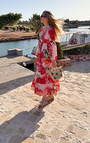 italienische mode kleiber werksverkauf Frau in einem geblümten Maxikleid mit Strohtasche am Wasser