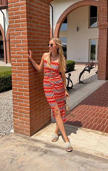 italienische mode kleiber werksverkauf Frau in rot-blau gestreiftem Kleid und Sandalen vor Ziegelwand