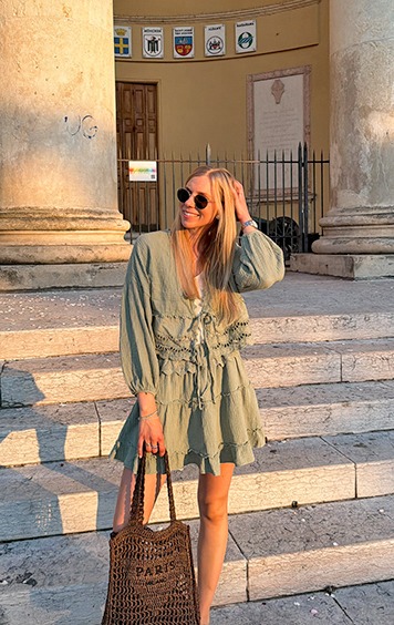 italienische mode kleiber werksverkauf Frau in einem grünen Kleid mit Tasche vor einer Säule