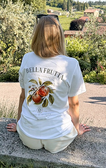 italienische mode kleiber werksverkauf Frau trägt T-Shirt mit Aufdruck „Bella Frutta“ und Pfirsichmotiv