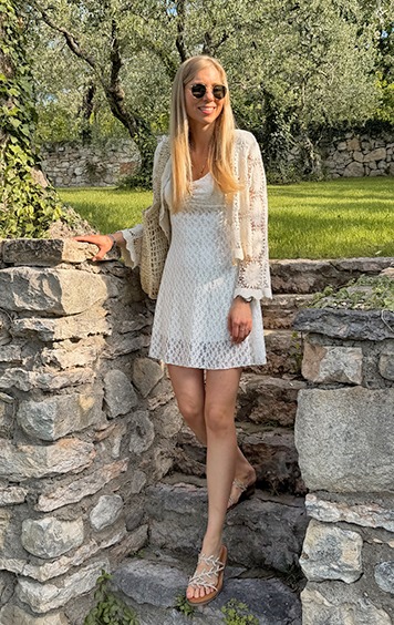 italienische mode kleiber werksverkauf Frau in weißem Kleid und Häkeljacke in sonniger Gartenlandschaft