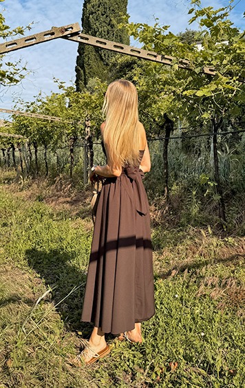 italienische mode kleiber werksverkauf Frau in braunem Kleid steht in einem Weingarten.