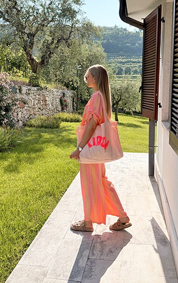 italienische mode kleiber werksverkauf Frau mit rosa-gestreiftem Outfit und LIRIDA-Tasche in sonniger Gartenlandschaft