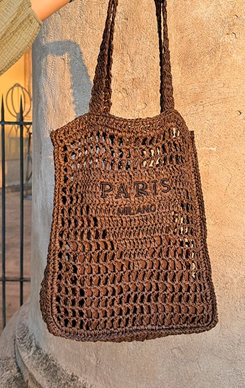 italienische mode kleiber werksverkauf Braune gehäkelte Tasche mit „PARIS MILANO“ Aufdruck, gehalten von einer Person
