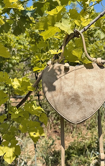 italienische mode kleiber werksverkauf Herzförmige Tasche aus Wildleder hängt an Weinrebe im Sonnenlicht
