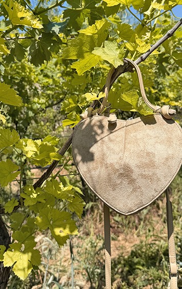 italienische mode kleiber werksverkauf Herzförmige Tasche aus Wildleder hängt an einem Ast mit Blättern