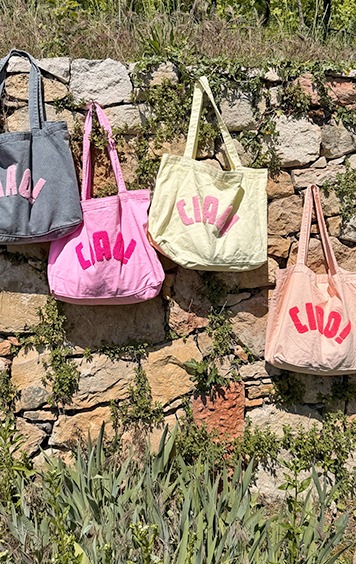 italienische mode kleiber werksverkauf Vier bunte Stofftaschen mit "Ciao!" Aufschrift hängen an einer Steinmauer.