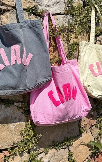italienische mode kleiber werksverkauf Drei bunte "Ciao"-Taschen aus Stoff hängen an einer Steinmauer.