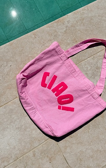 italienische mode kleiber werksverkauf Pink tote bag with "ciao" lettering lies on a tiled surface near a pool