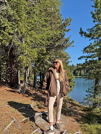 italienische mode kleiber werksverkauf Frau mit brauner Jacke und Beigefarbenem Outfit am See in den Bergen