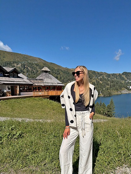 italienische mode kleiber werksverkauf Frau in weißer Kleidung vor Bergkulisse mit See und Hotel