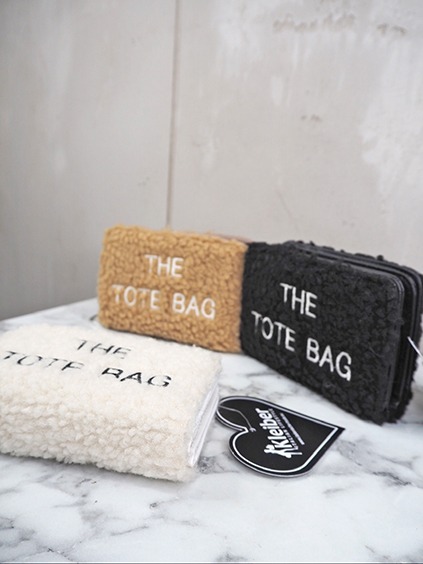 italienische mode kleiber werksverkauf Drei Teddy-Taschen mit der Aufschrift "THE TOTE BAG" in Beige, Schwarz und Creme.