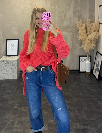 italienische mode kleiber werksverkauf Frau im pinken Oversize-Strickpullover und Jeans nimmt Selfie auf.