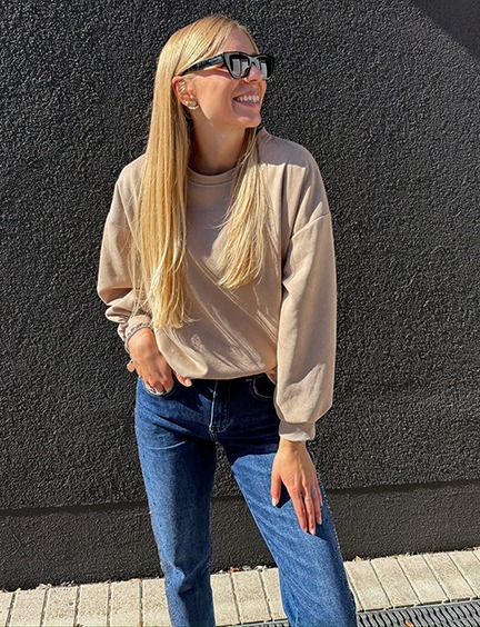 italienische mode kleiber werksverkauf Frau in beigem Pullover und Jeans lächelt.