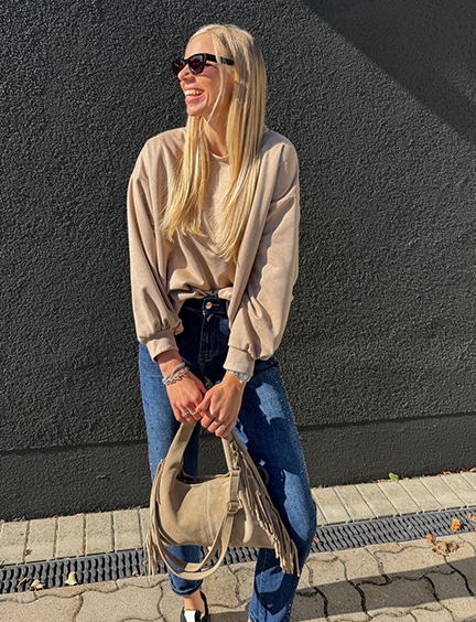 italienische mode kleiber werksverkauf Frau in beiger Oversize-Pullover, Jeans und Fransen-Tasche, Herbstmode