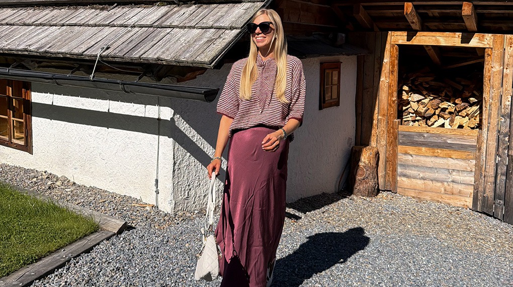 italienische mode kleiber werksverkauf Frau in langem Sommerkleid vor rustikaler Berghütte mit Holzstapel