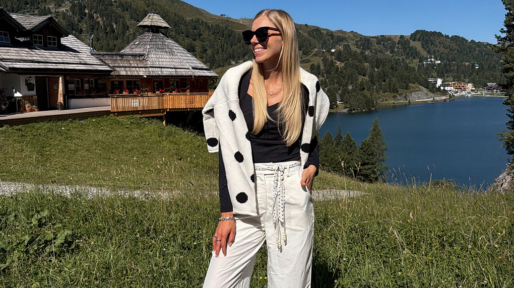 italienische mode kleiber werksverkauf Frau mit Sonnenbrille und weißer Hose vor Bergsee und Alpenhaus