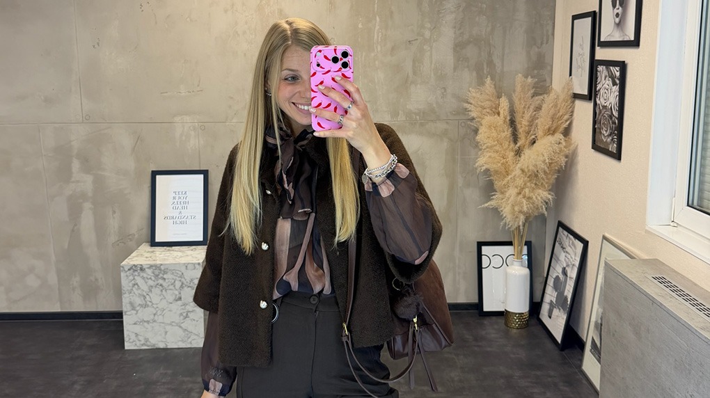 italienische mode kleiber werksverkauf Frau im modischen Outfit mit braunem Blazer und Bluse, hält Smartphone.